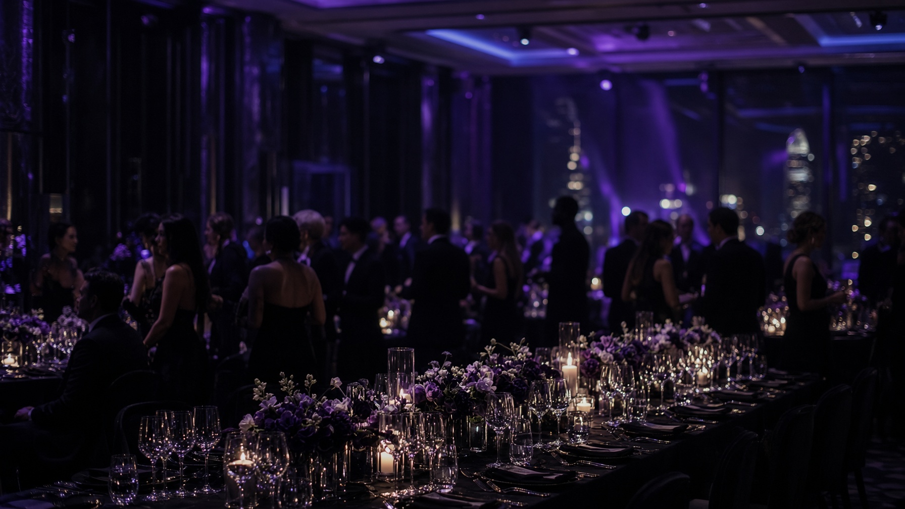 A dark ballroom set for a seated gala, lit with violet light